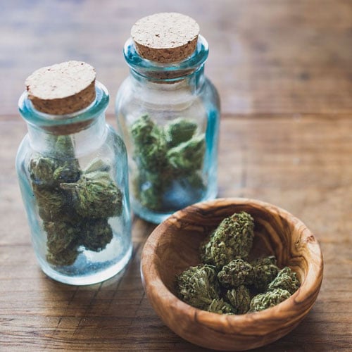 Medical marijuana inside glass containers with more marijuana in a wooden bowl next to it